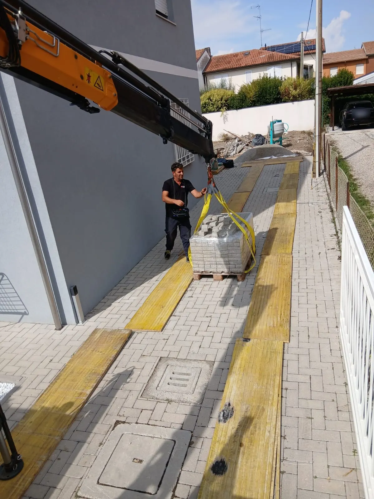 Autocarro con gru che scarica un bancale di autobloccanti in un cortile, su tavole che proteggono la pavimentazione