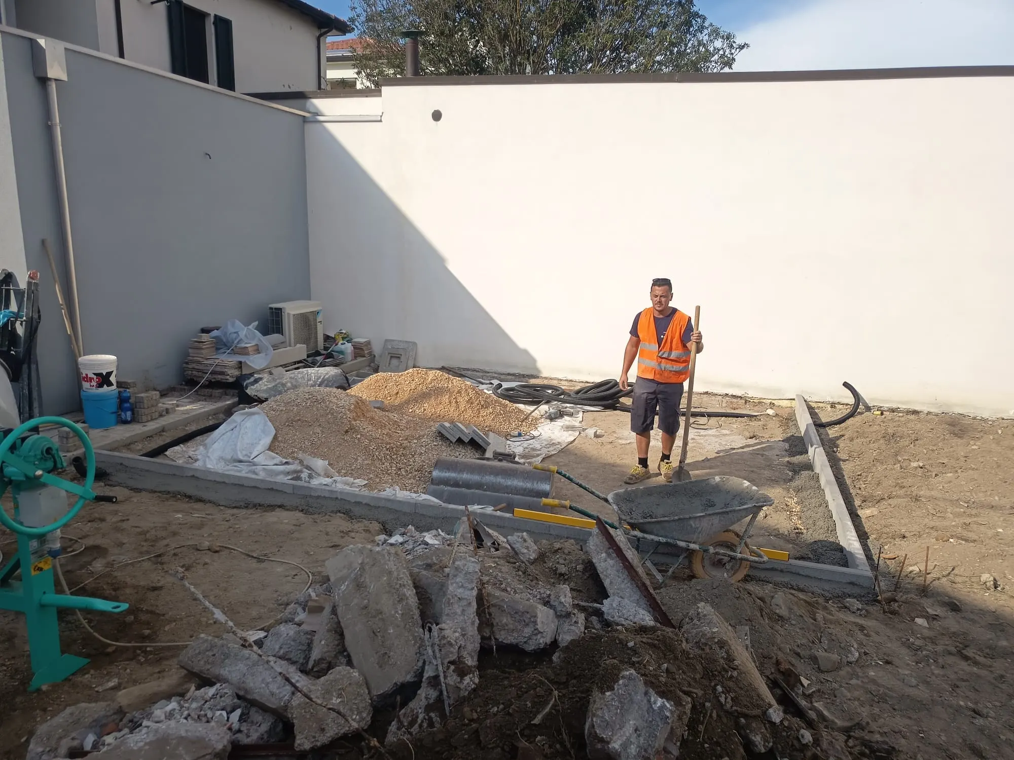 Cordoli posati e sottofondo in preparazione per una nuova pavimentazione, con cumuli di ghiaia e un operaio in cantiere