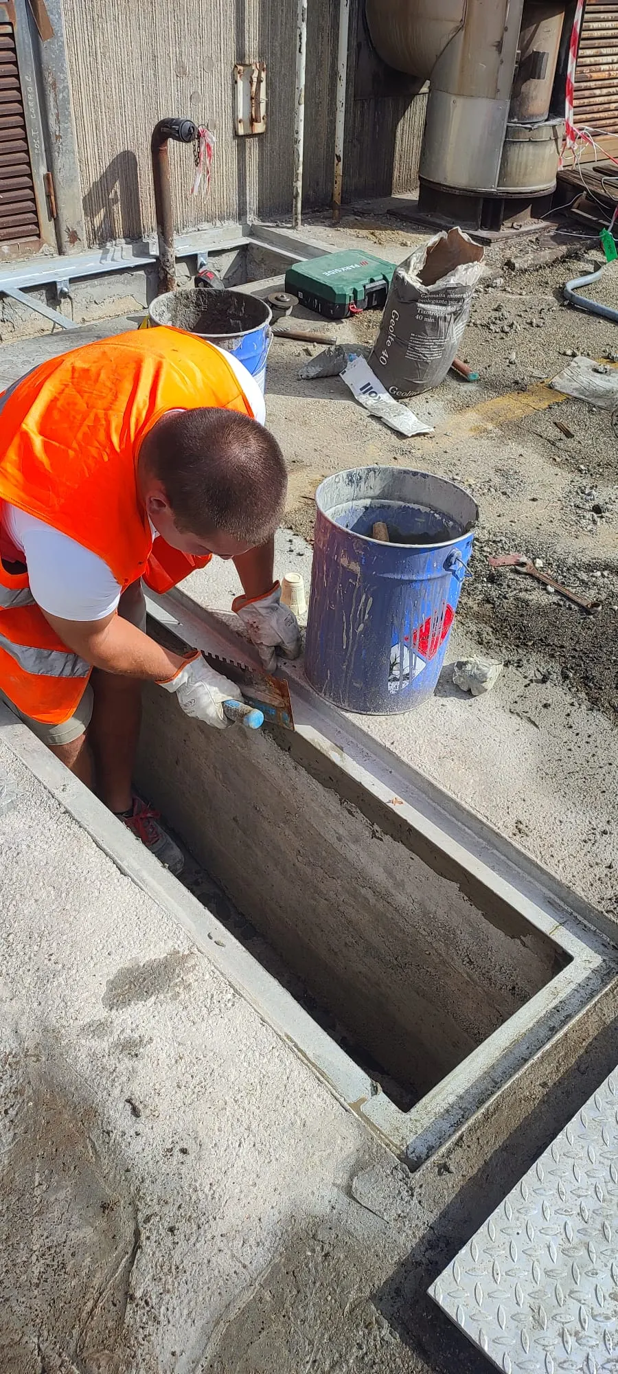 Operaio che rifinisce con la malta una canaletta in calcestruzzo in uno stabilimento