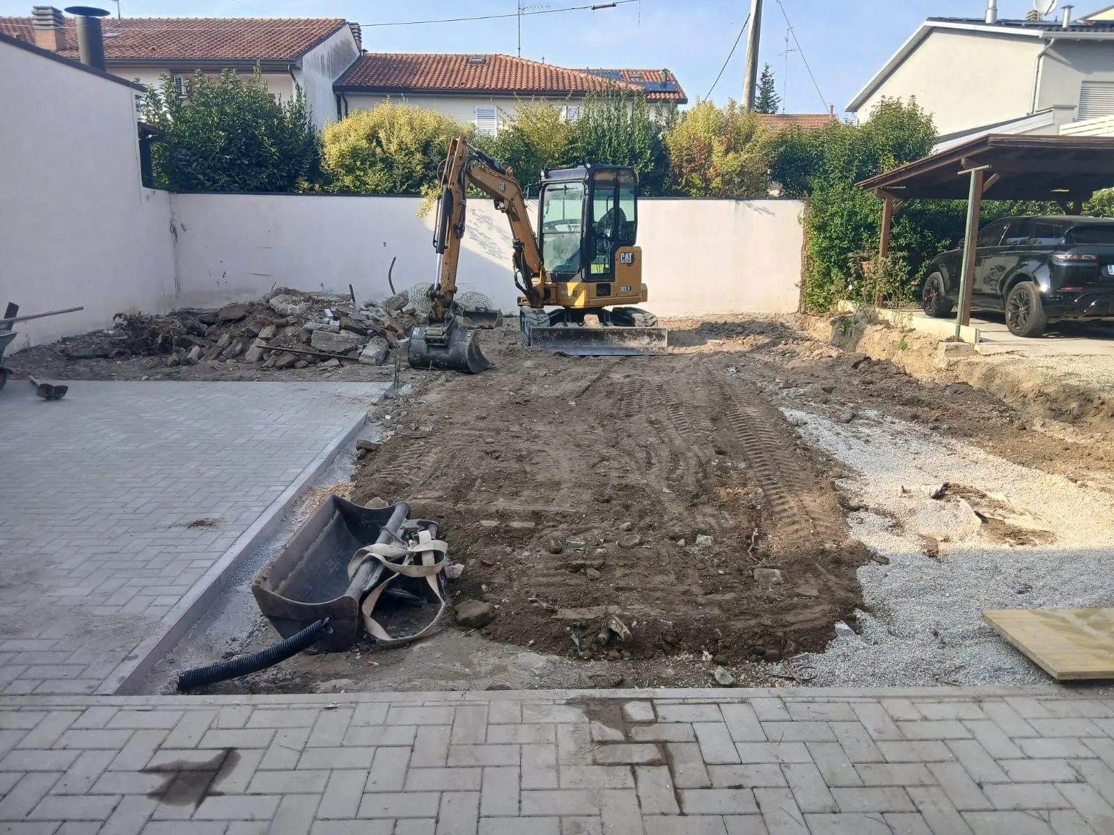 Miniescavatore in un cortile: il terreno è scavato e livellato accanto alla pavimentazione in autobloccanti